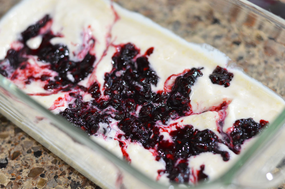 Glass loaf pan with one layer of ice cream topped with blackberry sauce