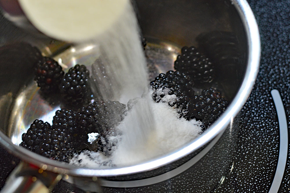 Adding sugar to fresh blackberries in a pan