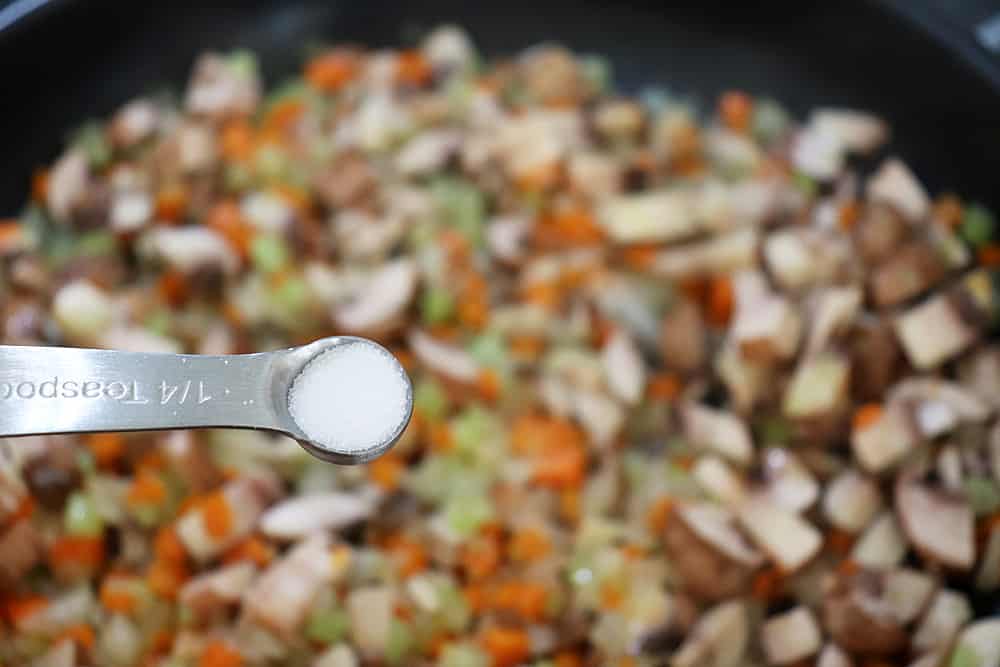 1/4 teaspoon of salt being added to sauteed vegetables