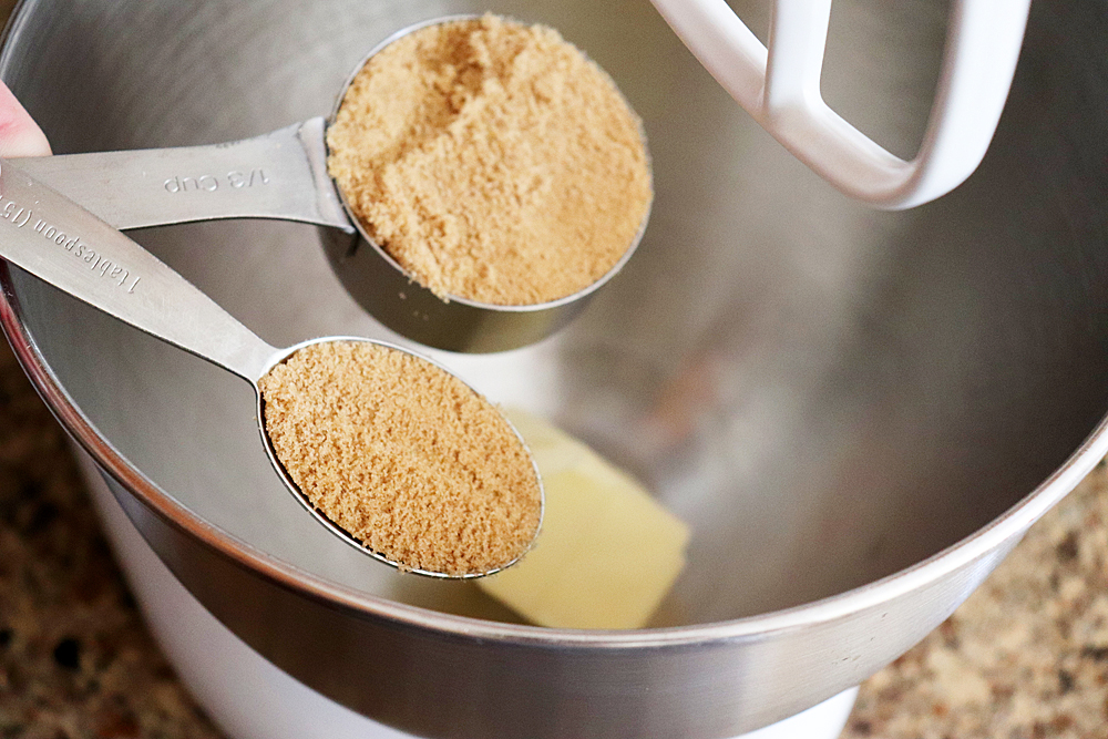 Measuring cup of brown sugar being added to butter in an electric mixer