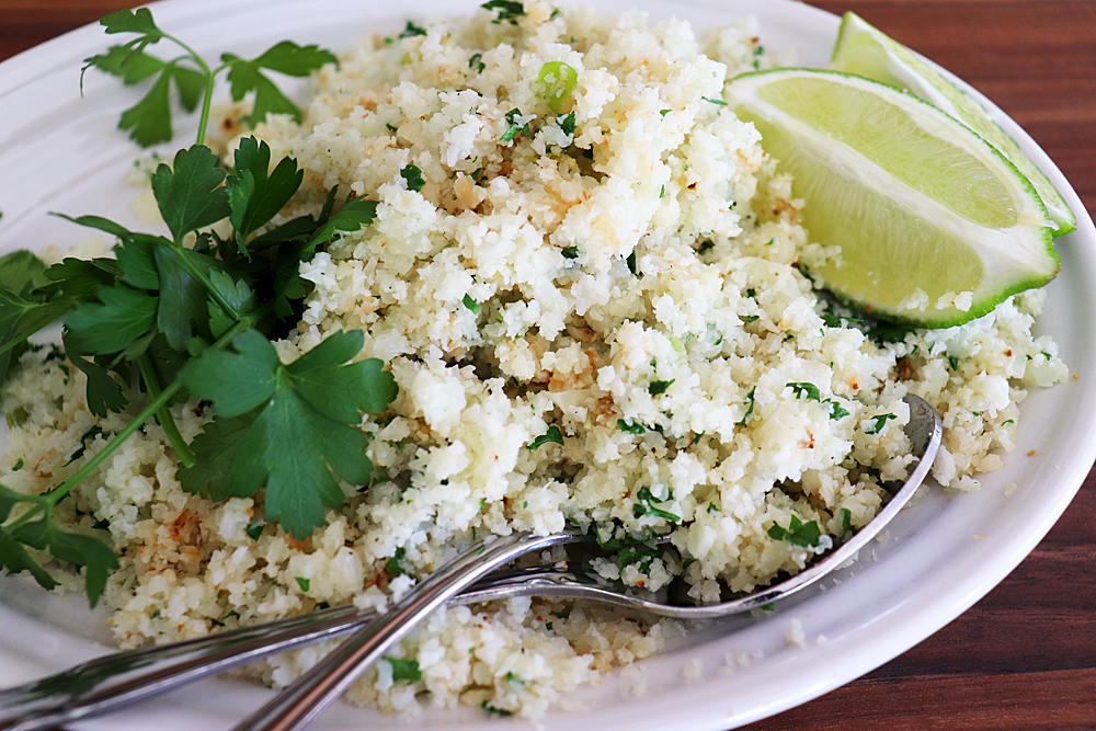 Close up of cauliflower rice on an oval white plate with two spoons