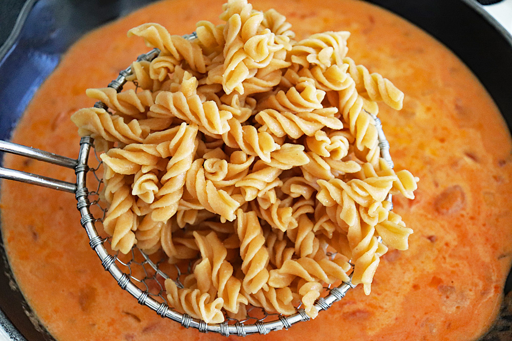 Adding cooked pasta to the tomato cream sauce