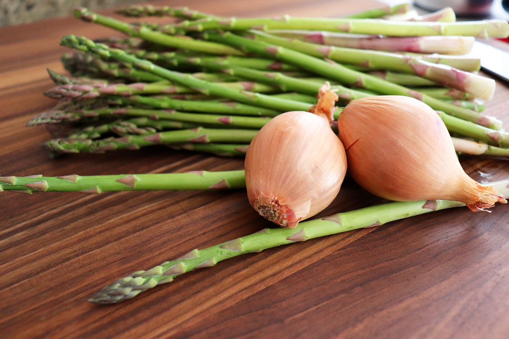 Photo of asparagus spears and shallots on a brown cutting board