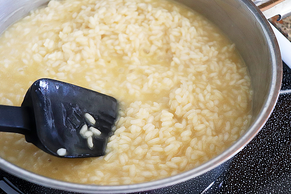 Risotto and broth in a pan with a black spatula
