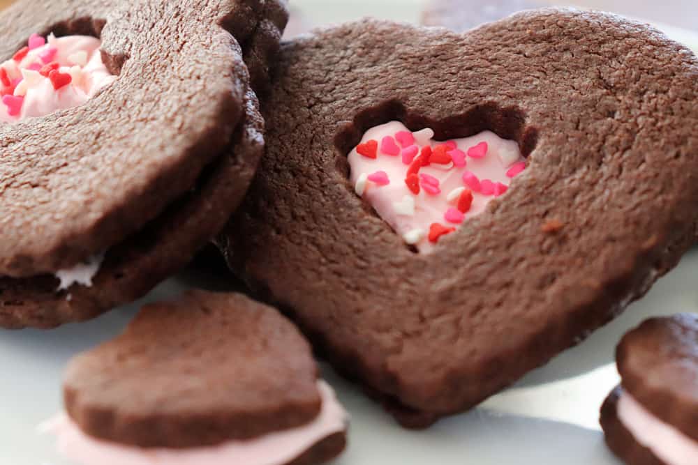 Close up of finished Vegan Chocolate Sugar Cookies frosted and decorated with tiny heart sprinkles